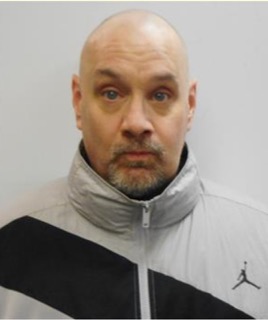 Man with shaved head and graying beard, wearing a gray and black puffer jacket