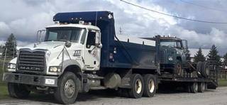 Two Mack trucks, one a dump truck, the other on a trailer.