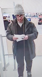 Person wearing a black coat, gray beanie, and glasses holds a small package.