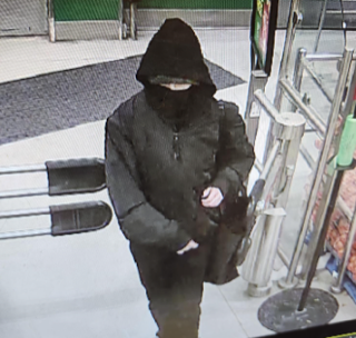 Person in dark hooded jacket and pants, face obscured, walking on pavement