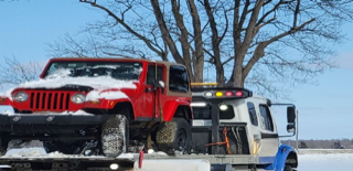 Red Jeep on a tow truck, covered in snow