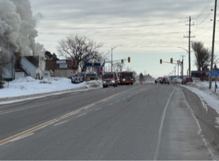 Fire trucks and smoke near a snow-covered street.