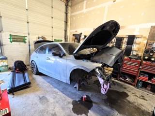 Blue sedan with hood and driver's side door open, showing engine components.