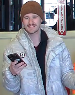 Man in a puffer jacket and knit hat smiles while holding a smartphone.