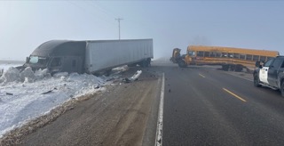 Semi-truck overturned on snowy roadside, school bus nearby, police vehicle visible