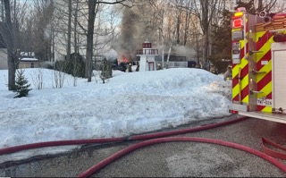 Firefighters and smoke rising from a house with snow-covered yard