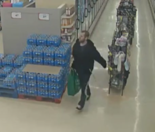 Man walking past pallets of bottled water, carrying a green bag.