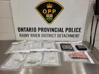 Ontario Provincial Police, Rainy River District Detachment. Several small plastic bags containing a green substance, Canadian fifty-dollar bills, and a smartphone on a metal surface.