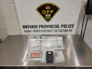 Ontario Provincial Police logo and text: Ontario Provincial Police, Rainy River District Detachment. Several baggies of a white powdery substance, Canadian currency, and a black smartphone on a metal surface.