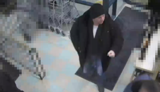 Person in a dark coat and hat walking across a tiled floor.