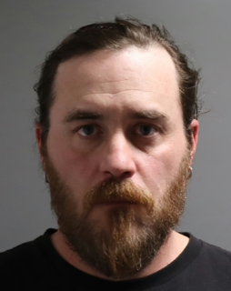 Man with a full reddish-brown beard and short dark hair.