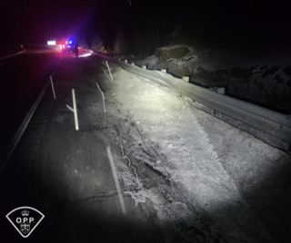 Road covered in snow and ice, emergency vehicles with flashing lights visible in the distance