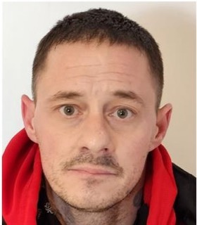 Man with short dark hair and a short beard looks directly at the camera.