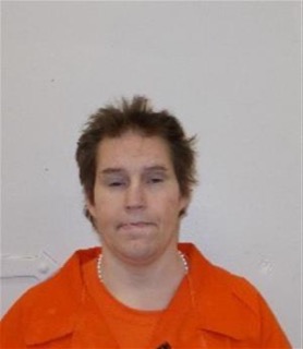 Person with short dark hair and a pearl necklace, wearing an orange shirt