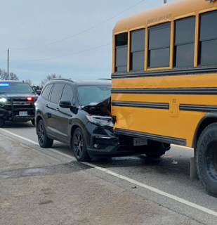 Black SUV damaged, rear-ended a school bus. Police vehicle visible in background.