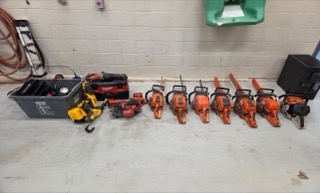 Six orange chainsaws lined up on a gray floor.