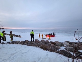 Rescuers and a hovercraft on a snow-covered shoreline.