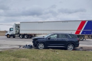 Damaged black SUV on grass, semi-truck in background