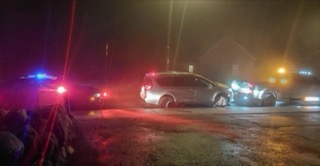 Several police vehicles surround a minivan in fog.