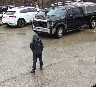 Person walking across a parking lot, black pickup truck and SUV visible in background