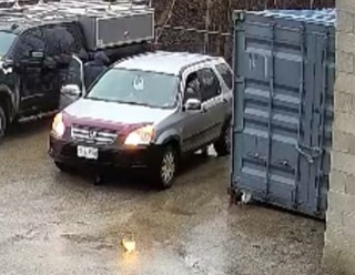 Silver minivan parked next to a blue shipping container.