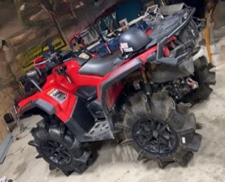 Red Can-Am ATV with large tires covered in mud