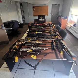 Numerous firearms displayed on a table.
