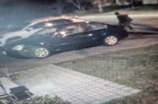 Black car parked on a driveway. A person is visible near the car.