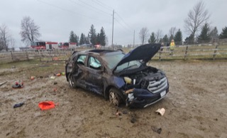Damaged blue SUV in muddy field, hood open, front end crushed