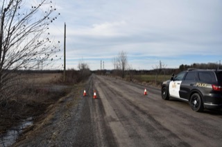 Police vehicle on a gravel road, traffic cones, bare trees, overcast sky