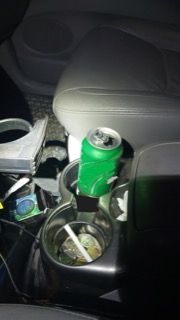 Green soda can in a cup holder, coins and trash visible