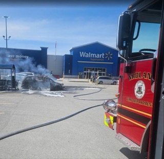 Damaged car with smoke, fire truck on scene, Walmart in background