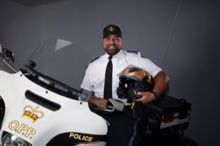 Police officer in uniform stands in front of a marked police motorcycle.