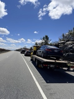 Black sedan on a tow truck, highway background