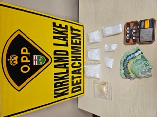 OPP logo and Kirkland Lake Detachment text on a yellow sign. Packages of a white substance and Canadian twenty-dollar bills.