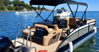 Pontoon boat on blue water, two outboard motors, cushioned seating, black canopy, two people in the distance