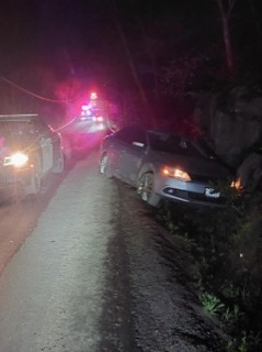 Car partially off a gravel road, pink and red emergency lights in the background