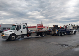 White car carrier truck parked in a lot, Staples store in background