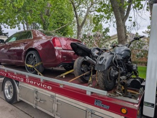 Damaged motorcycle on a tow truck bed, next to a red car