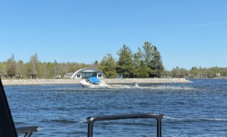 Boat speeding across a lake, wake visible behind it. Trees and a dome-shaped building on the shoreline.