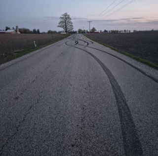 Tire marks swirl across a dark asphalt road.