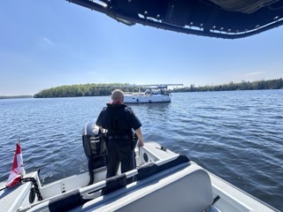 Man operating a boat on a lake, evergreen trees lining the shore