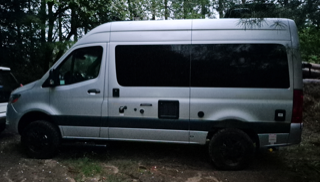 Silver Sprinter van with black wheels and side steps.