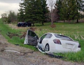 Damaged white sedan in tall grass, front end crushed