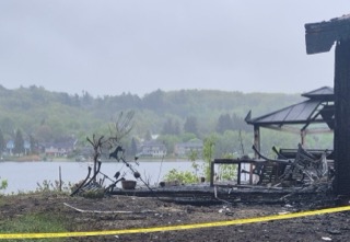 Burned building with yellow caution tape. Green trees and houses across a lake.
