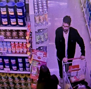 Man wearing a black jacket and glasses, pushing a shopping cart in a store.