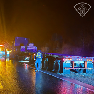 Semi-truck on wet road, two people in high-visibility vests standing nearby